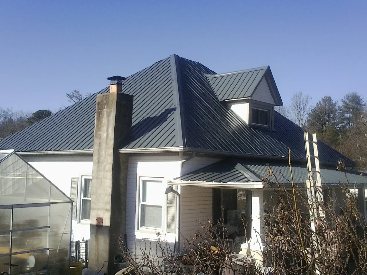Dark blue standing seam metal roof on a white farmhouse with dormer — Slate & Tile Roof Repair by Roofing Brothers in Blachly