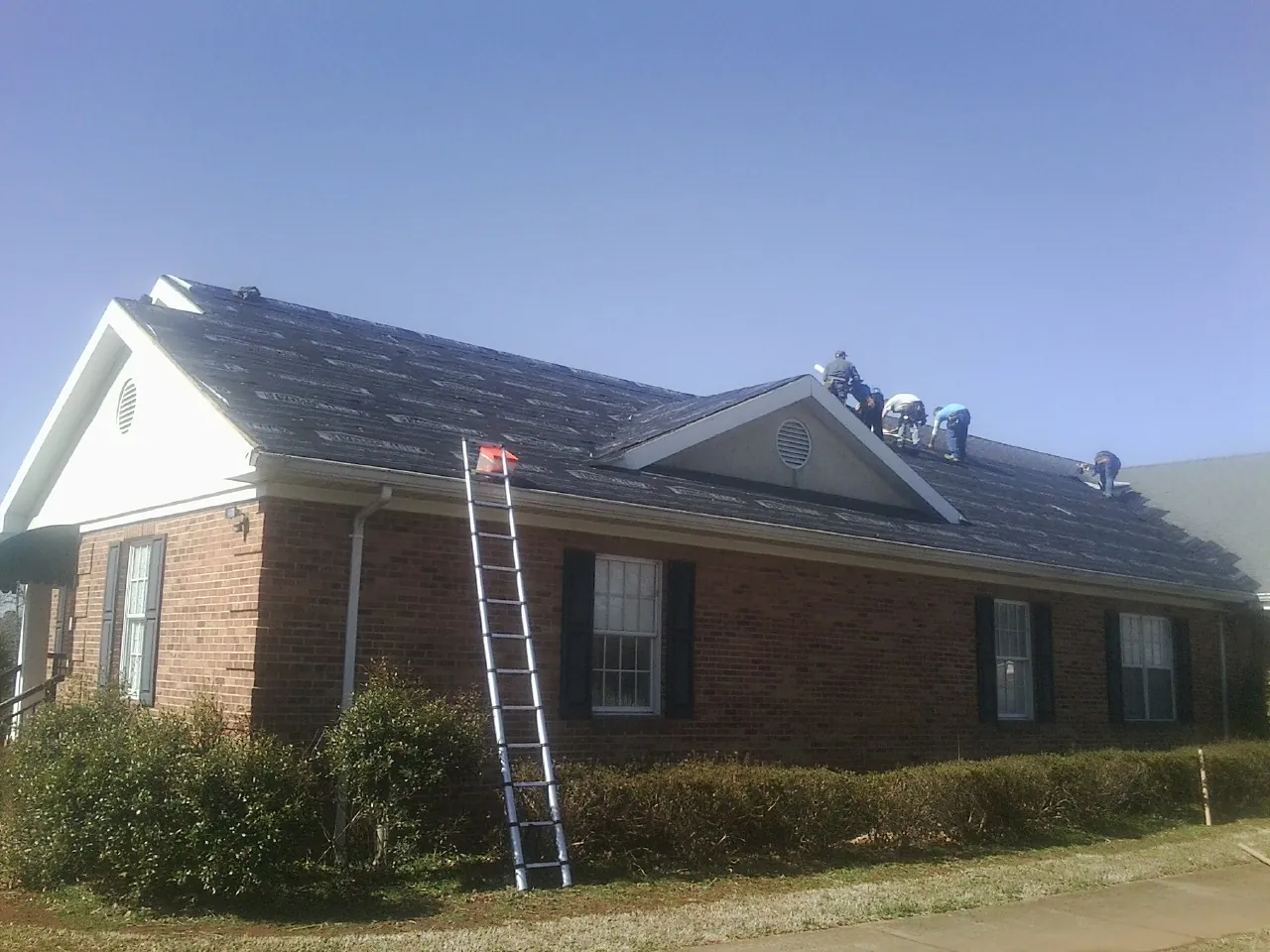 Crew tearing shingles off a brick ranch roof with a ladder set — Metal Roof Repair work by our crew in Blachly