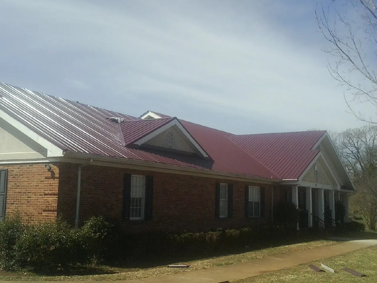 Red metal roof with gabled entries on a long brick building, from a Hail Damage Roof Repair job in Blachly