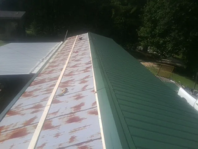 Old rusted panels beside newly installed green metal roofing — Wind Damage Roof Repair by Roofing Brothers in Blachly
