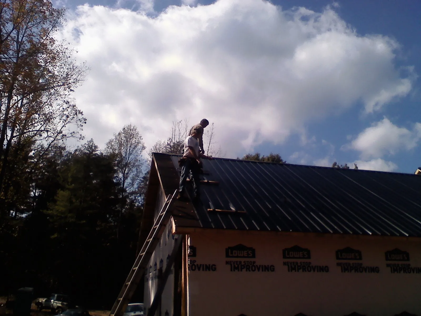 Roofer fastening dark metal panels high against a cloudy sky, from a Roof Inspection job in Blachly
